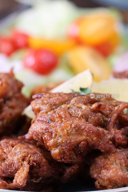 全帧图像的餐盘，包括自制的脆洋葱bhajis / pakoras，黄瓜片，樱桃番茄，红洋葱圈，raita和酸辣酱蘸酱，印度菜素食小吃，聚焦前景